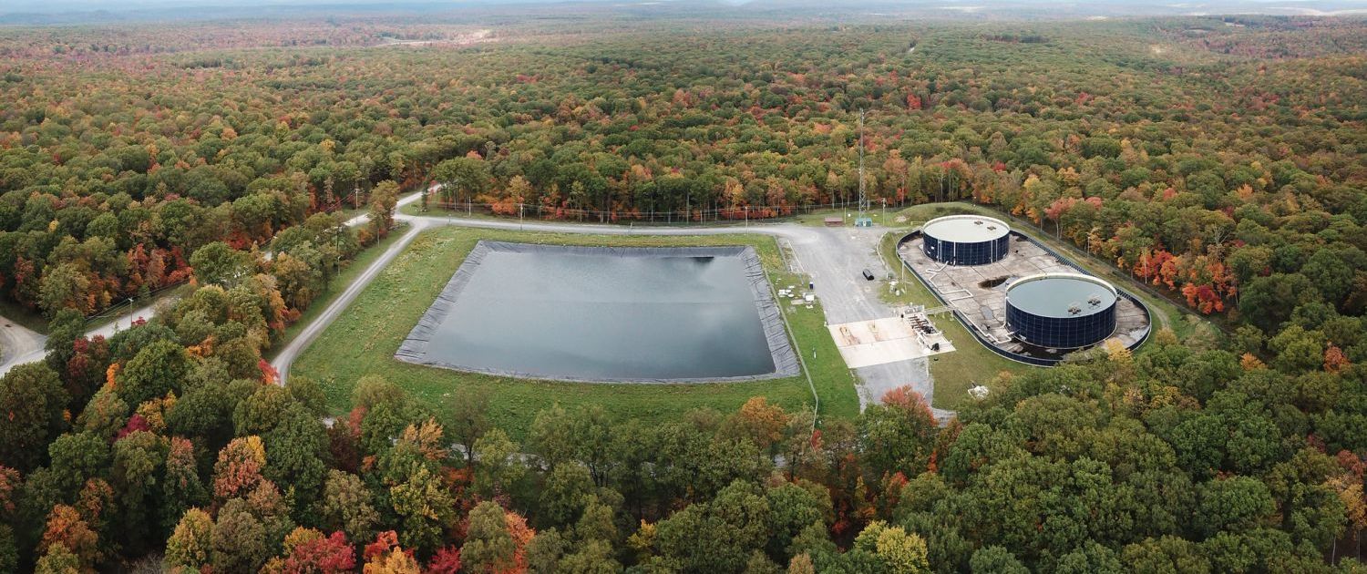 Aerial view of a lined water impoundment and two storage tanks at a Seneca Resources site in Clearfield County, Pennsylvania, surrounded by autumn forest.