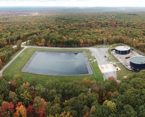 Aerial view of a lined water impoundment and two storage tanks at a Seneca Resources site in Clearfield County, Pennsylvania, surrounded by autumn forest.