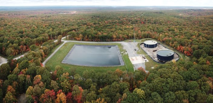 Aerial view of a lined water impoundment and two storage tanks at a Seneca Resources site in Clearfield County, Pennsylvania, surrounded by autumn forest.