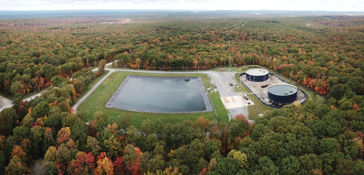 Aerial view of a lined water impoundment and two storage tanks at a Seneca Resources site in Clearfield County, Pennsylvania, surrounded by autumn forest.