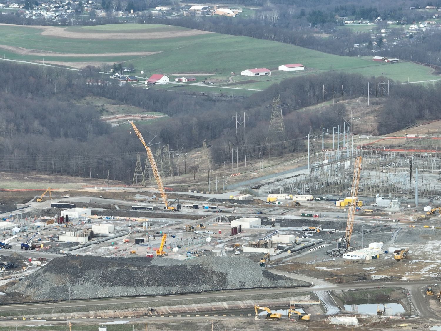 Aerial view of cranes, foundations, and a substation under construction at the Homer City Energy Campus, with farms and houses on the hills behind.